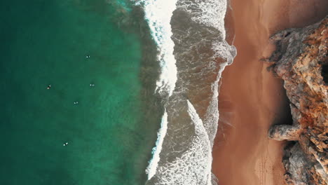 Luftaufnahme-Von-Klippen-Zum-Ozean-Mit-Surfern,-Die-Auf-Wellen-Warten
