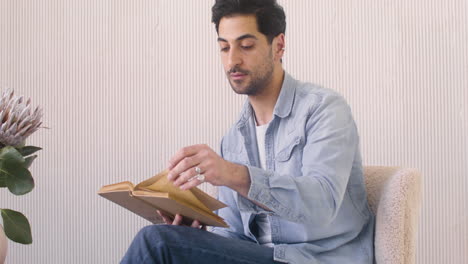 hombre de cabello oscuro leyendo un libro en casa