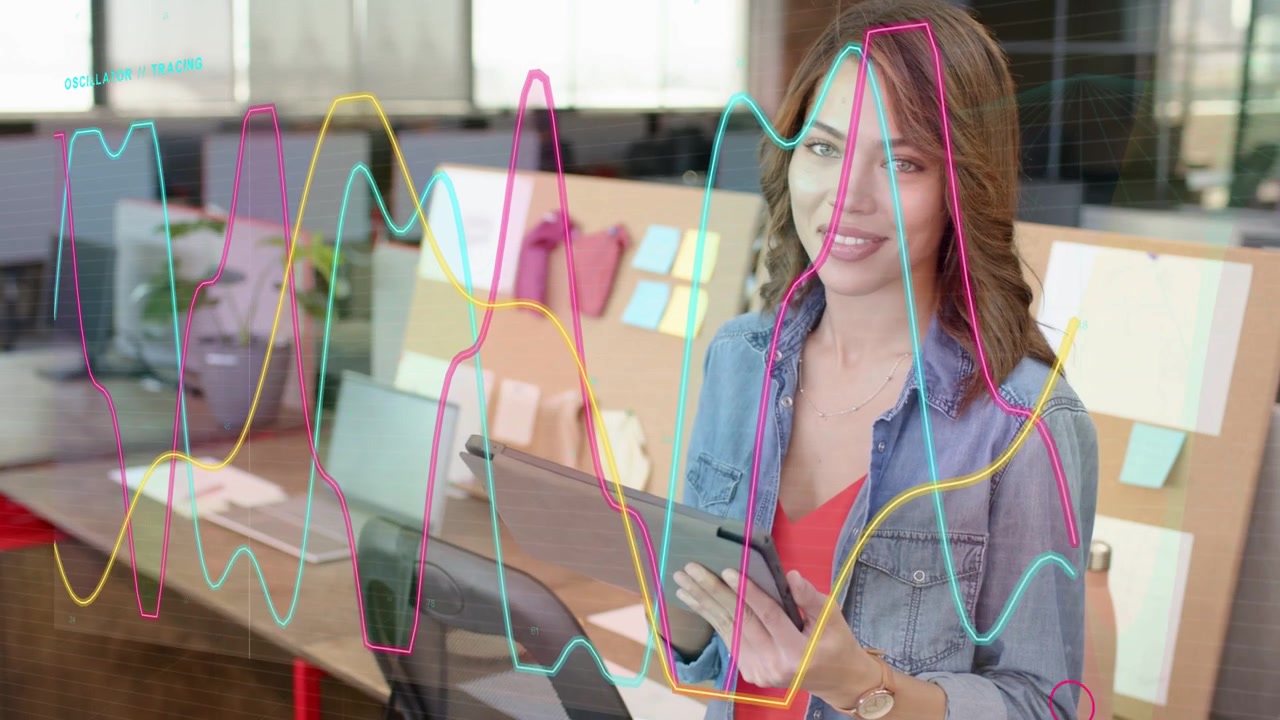 Woman tapping tablet at creative studio, causing moving line graphs crossing desk, leading to smile