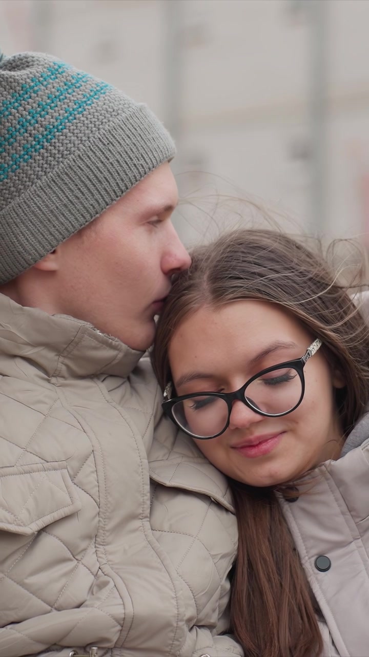 La presenza di una donna è notata da un uomo che indossa un cappello a righe vicino a lei. La compagna appoggia la testa sulla sua spalla e indossa gli occhiali. L'ambientazione mostra strutture fuori fuoco con una messa a fuoco morbida.