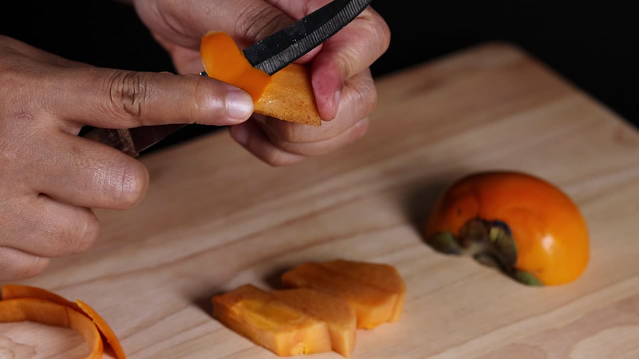 Hands slicing persimmon on wooden cutting board