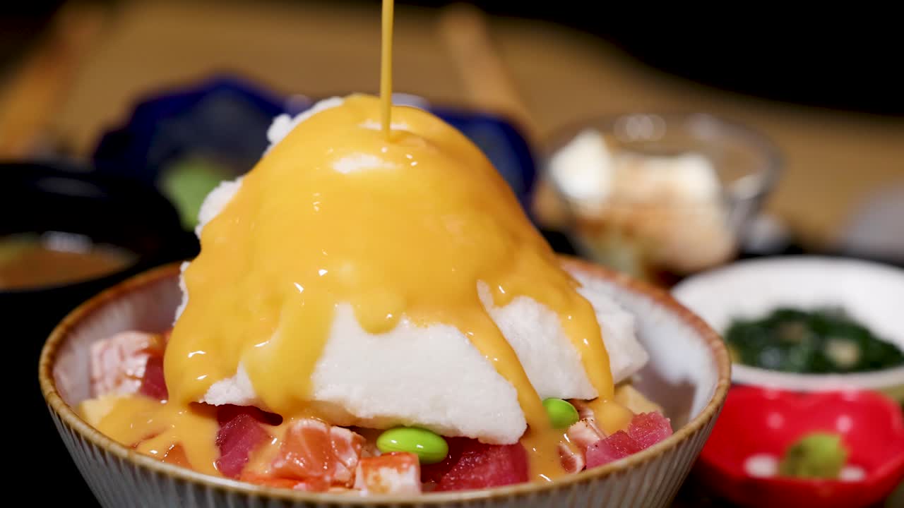Close-up saus keju krim yang dituangkan di atas mangkuk nasi hidangan laut chirashi dalam pencahayaan restoran yang hangat