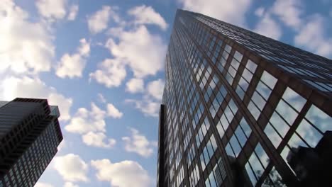 a dramatic perspective of tall glass buildings reaching for the sky, with fluffy clouds creating a vibrant backdrop. this urban landscape captures the essence of city life and architecture.