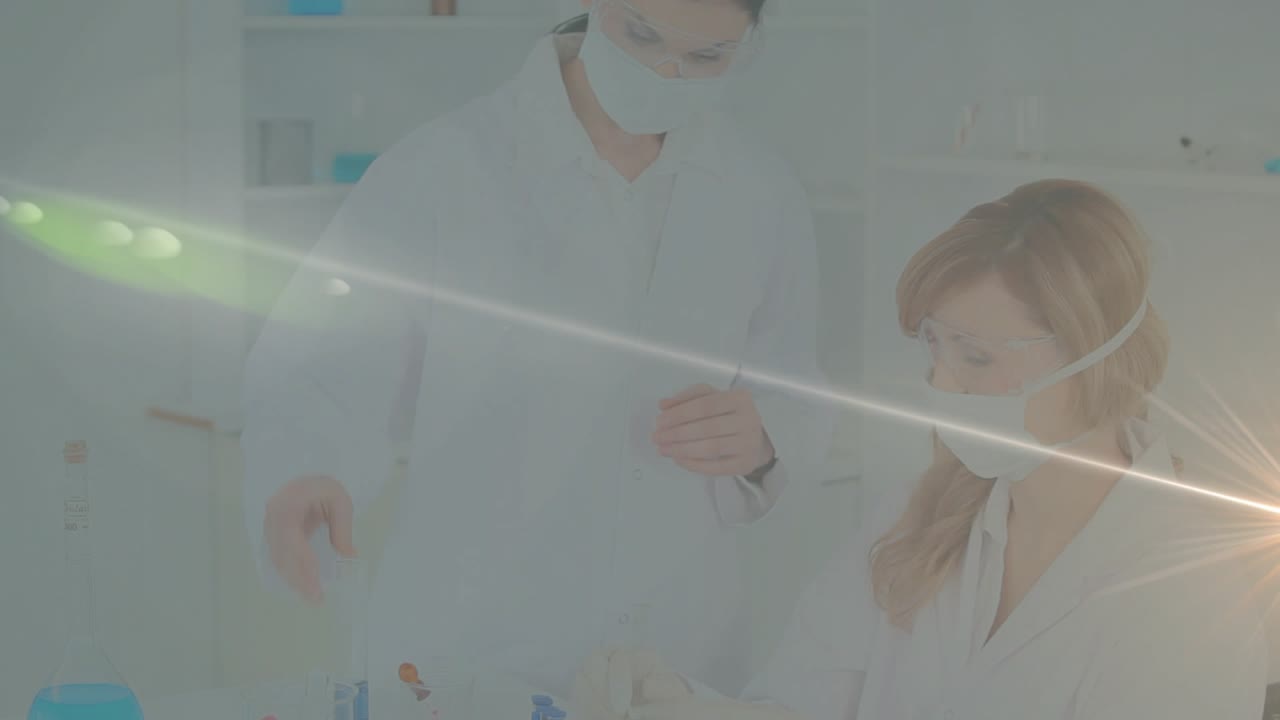 レンズフレアが差し込む中、科学者が研究室の顕微鏡を調整し、同僚がバイアルのサンプルを検査している。