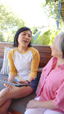vertical video: smiling woman holding tablet, talking with senior woman on outdoor patio