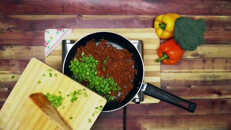 a top view of adding the capsicum in to the ingredients in pan, placed on a stove, two big yellow and red capsicums and a green broccoli on the table