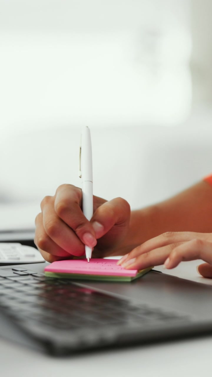 Person Writing on Pink Sticky Note at Desk