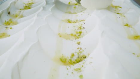 close-up of a creamy mascarpone ice cream with pistachio pieces while a scooper portions it out