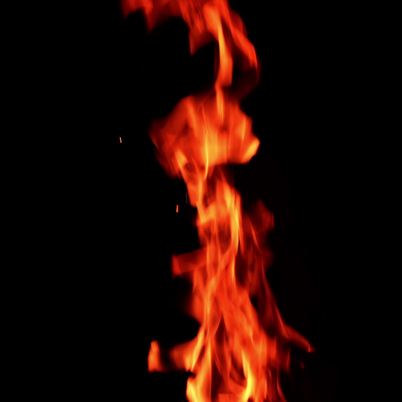 Long and thin flame of the fire burning in the darkness isolated. Tiny sparkles rise up in the air