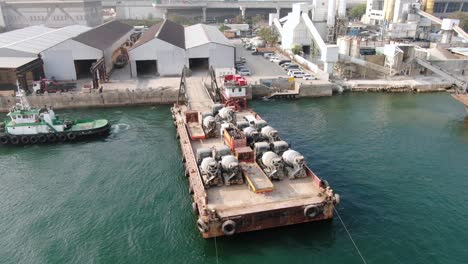 Barge-loaded-with-Concrete-mixer-trucks-pulled-to-port-by-a-Tugboat-in-Hong-Kong-bay,-Aerial-view