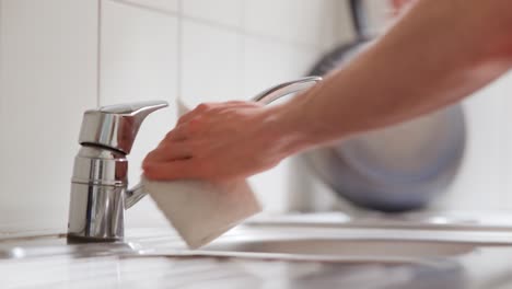 man wiping a kitchen tap with a cleaning wipe