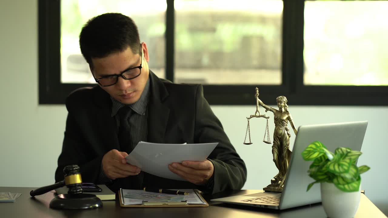 concept of justice and law A male lawyer works in an office with a brass scale goddess on a wooden table. Justice hammer with laptop Legal Concepts and Legal Services