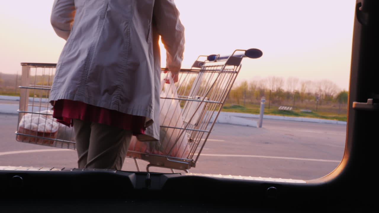 여자는 주차장에 있는 자동차 트렁크에 있는 상점에서 패키지를 저장합니다.