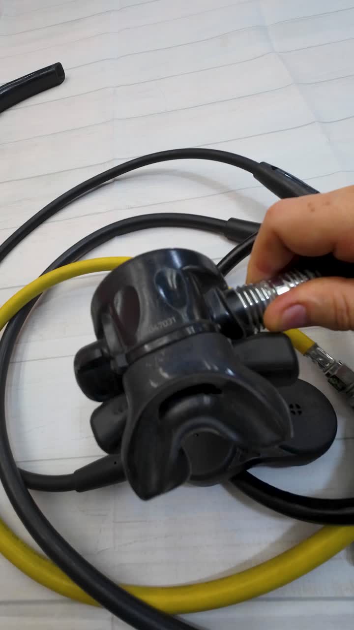 Main focus is on second stage regulator and the yellow hose connected to it. Details and connections of the gear, preparation or maintenance before a dive. Water sports