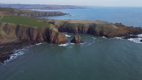 Flying-over-the-ocean-towards-the-cliffs-in-a-landscape-covered-by-green-grass