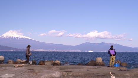 two fishermen fishing at pier with backdrop of mount fuji in japan