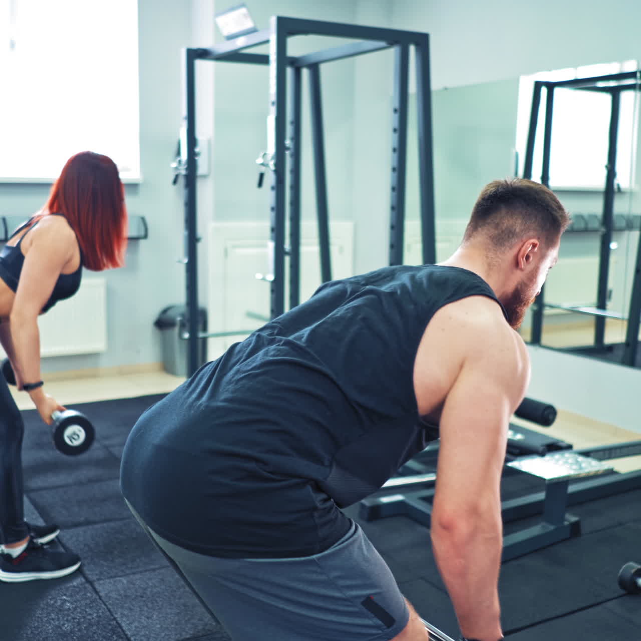 Athletic woman and man in sportswear lifting barbell in the gym. Persistent couple doing hard workout with heavy equipment standing in front of the mirror in modern sports club.