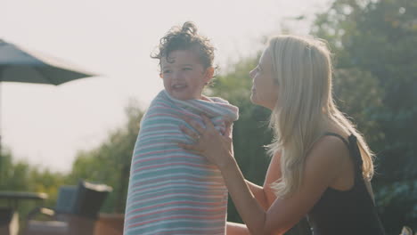 Mother-Wrapping-Young-Son-In-Towel-By-Outdoor-Swimming-Pool-On-Summer-Vacation