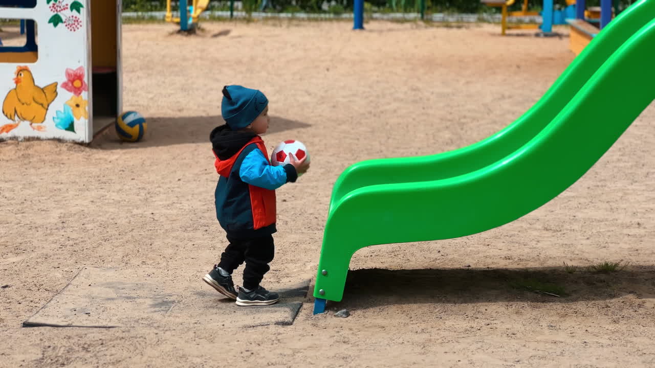 Adorable little toddler takes his ball to the slide. Kid pushes and catches the ball again.