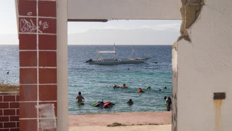 people swimming view from a ruined structure at the beachside of moalboal municipality in cebu, philippines. static shot