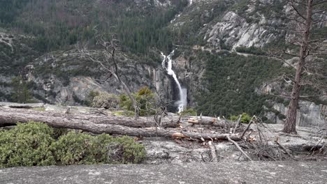 Approaching-Sentinel-Falls-in-Yosemite-National-Park-California-from-cliff-with-fallen-tree,-Aerial-dolly-in-shot