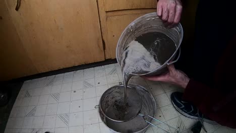 slow motion - dumping a bucket of mud into a strainer on the kitchen floor to remove the water