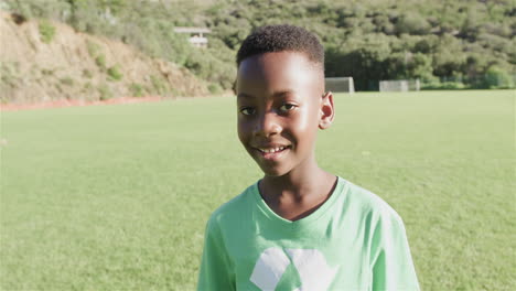 Un-Niño-Afroamericano-Sonríe-En-Un-Soleado-Campo-Al-Aire-Libre-Con-Una-Camiseta-Verde-De-Reciclaje