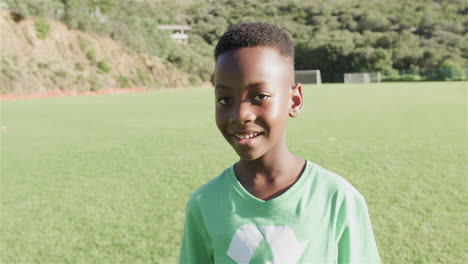 african american boy smiles on a sunny outdoor field wearing a green recycling t-shirt