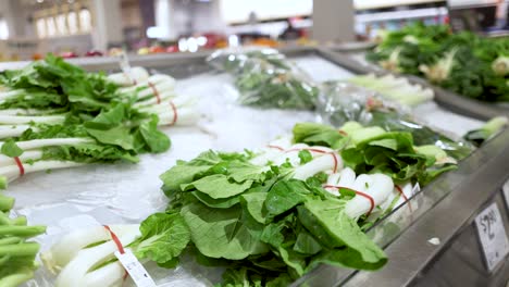 a hand picks bok choy from a well-lit supermarket display, showcasing fresh produce in a clean environment