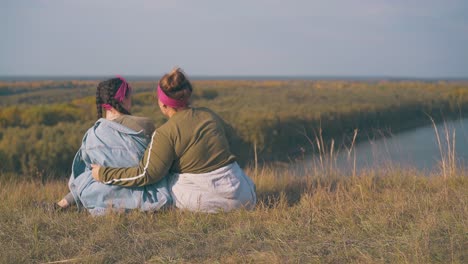 Una-Pareja-De-Lesbianas-Entusiasmada-Se-Sienta-En-La-Orilla-Del-Río-En-Otoño