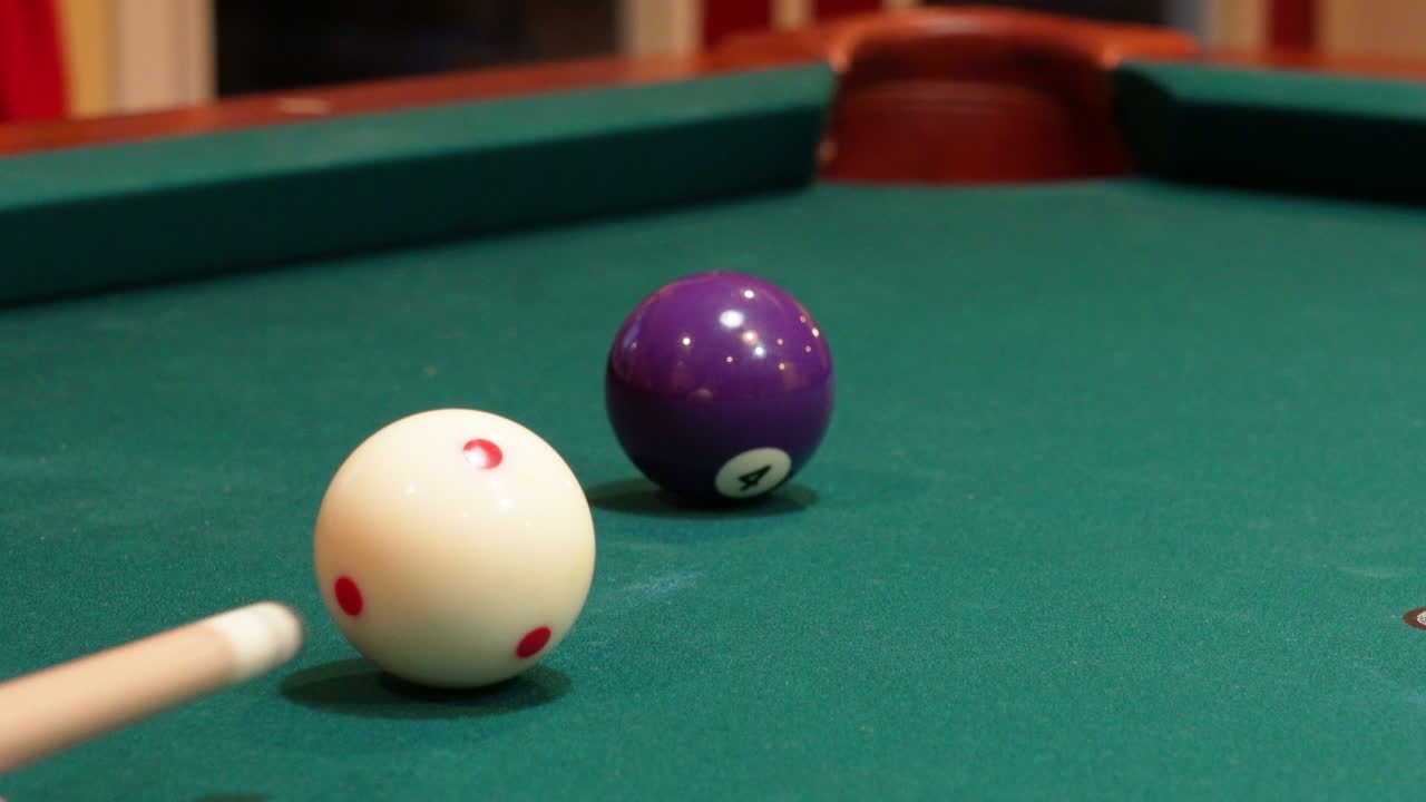 Closeup of Person Playing Pool Shooting Solid Purple 4 Ball into Corner Pocket after Practice Strokes using Cue Ball with Red Spots, Open Bridge Hand with Wooden Cue Stick and Green Felt or Cloth