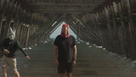 two masked people dance under the legs of a pier