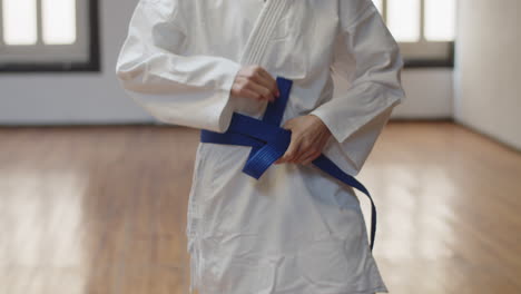 vista frontal de una chica irreconocible atando un cinturón azul en un kimono