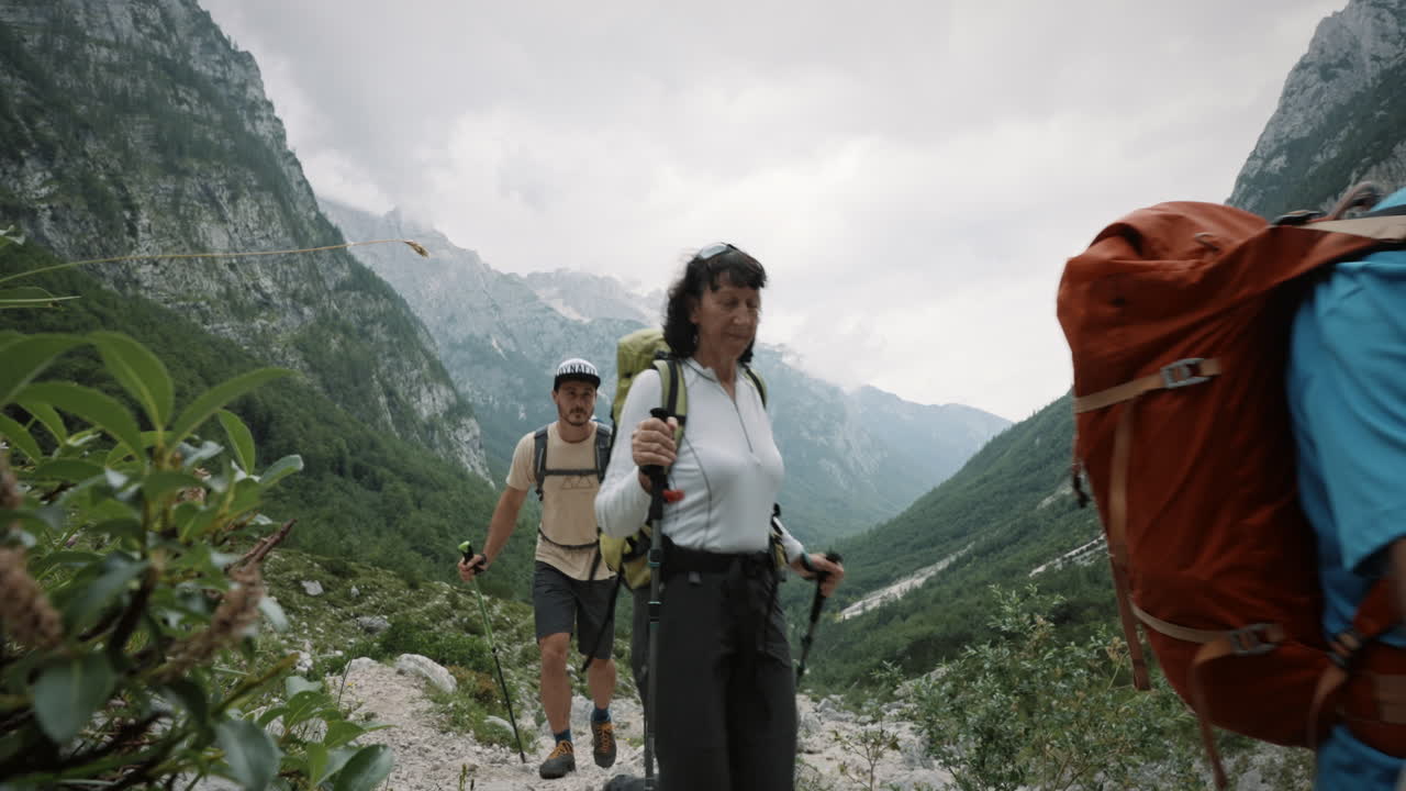 excursionistas pasando la cámara a la derecha, mirando hacia el valle verde y las altas montañas con couds que rodean los picos