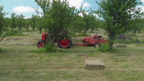 a farmer driving a hay baler between trees in a field