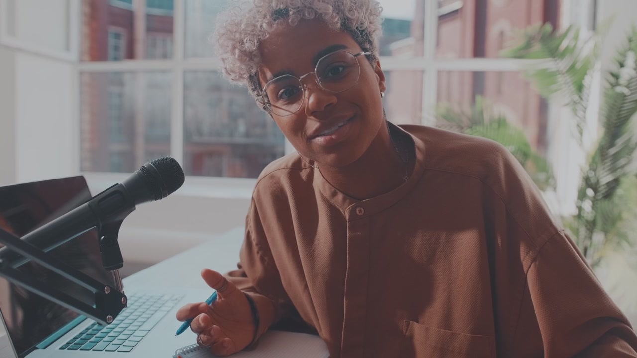 Ung afroamerikansk radiovært med hovedtelefoner sidder ved et skrivebord med en bærbar computer.