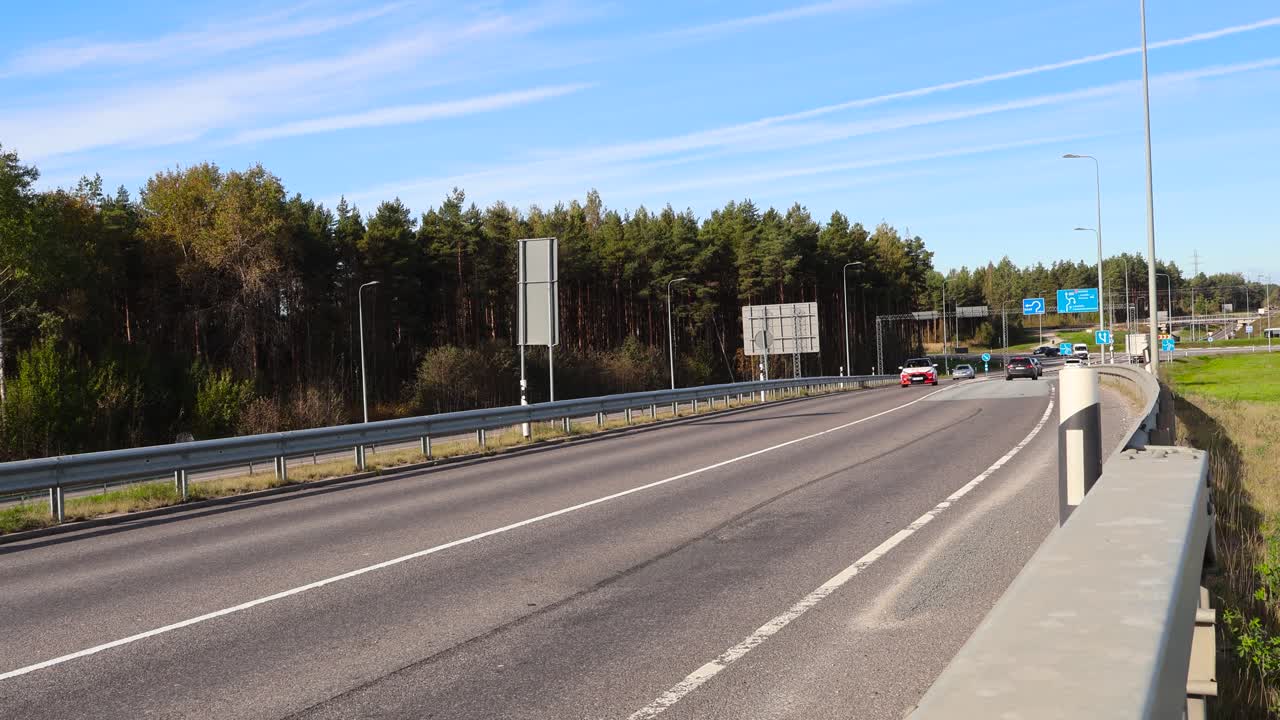 Cars, vehicles and trucks driving and moving to and from an overpass or a bridge going over Pärnu Highway in Laagri Estonia during a sunny day while some clouds are in the sky. Usual traffic on road.
