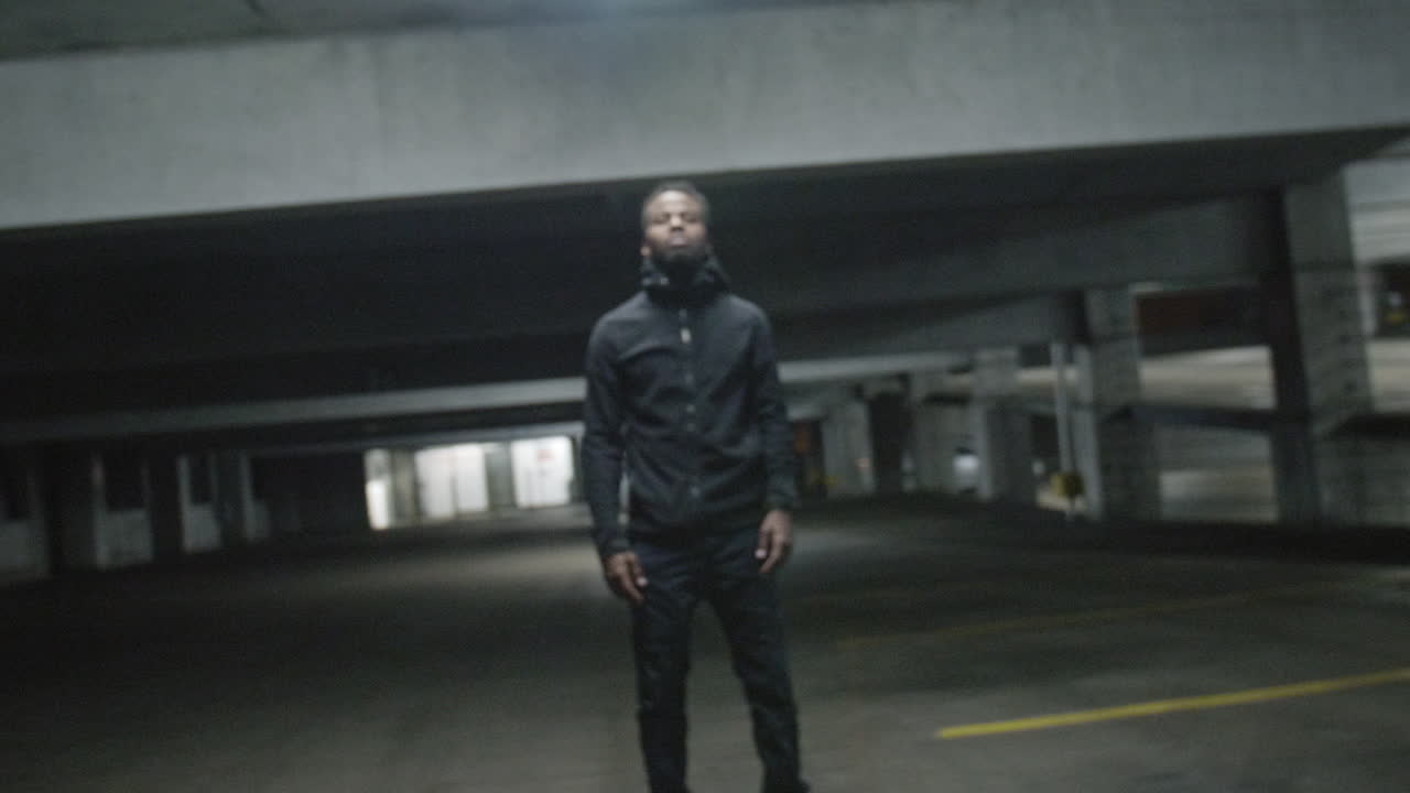 Zoom into an African American man standing still in a parking garage