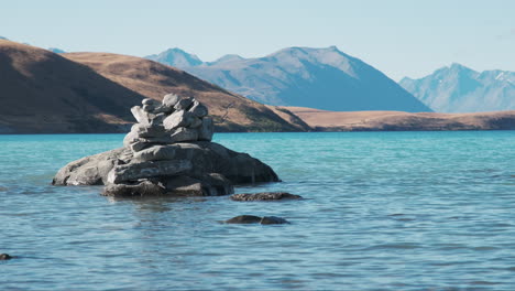 Rock-pile-made-by-tourists-in-the-stunning-aqua-turquoise-waters-of-Lake-Tekapo,-New-Zealand