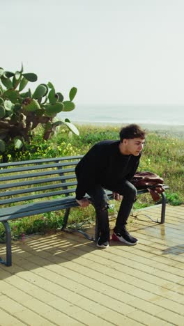 university student relaxing on a bench near the ocean
