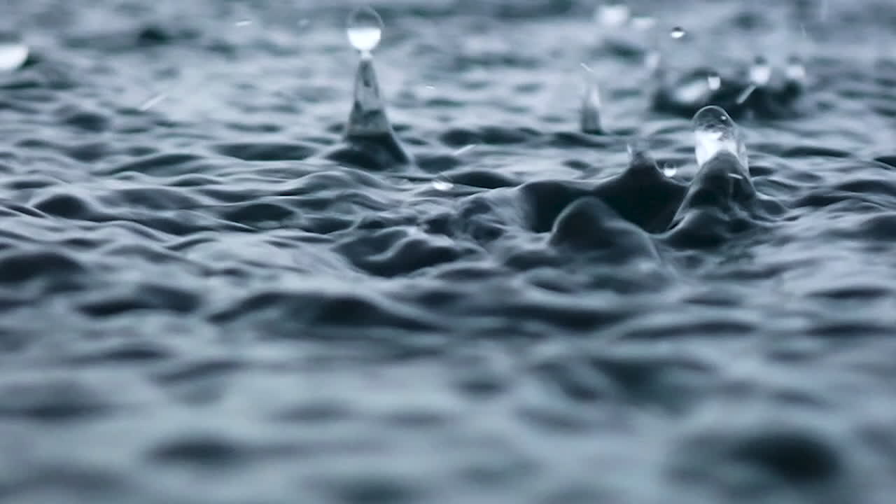 Slow motion of rain dropping into the endless ocean. It briefly bounces back to the air after it hits the sea surface.