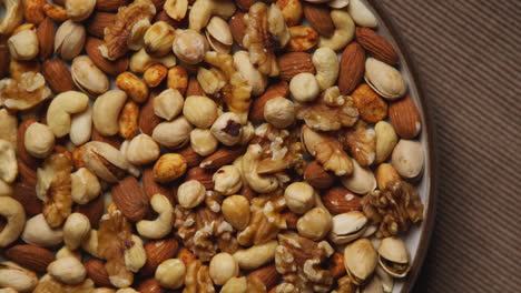 close up overhead shot of bowl containing cashews dry roasted peanuts pistachio walnuts and hazelnut nuts revolving