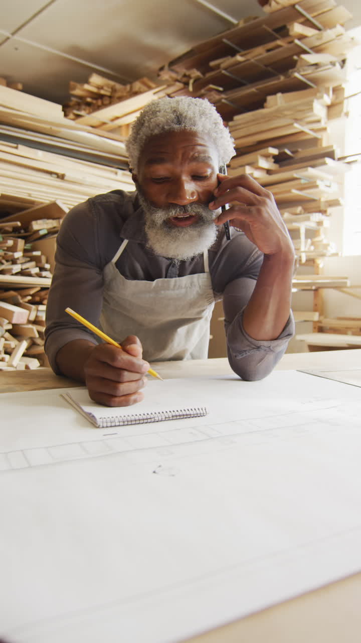 video vertical de un carpintero afroamericano de edad avanzada usando un teléfono inteligente en el taller