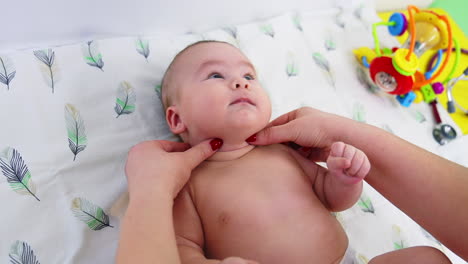 pediatrician touching and feeling baby's neck. little beautiful child lies peacefully during doctor's examination. toys at backdrop.