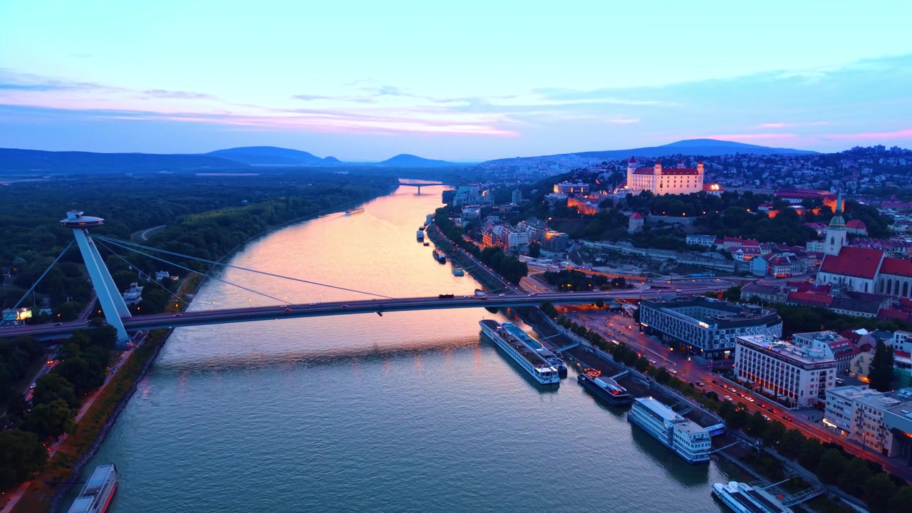Veduta aerea del Castello di Bratislava e del fiume durante un tramonto colorato. Veduta aerea del fiume che riflette la luce del tramonto con il castello, il ponte e l'argine della città durante la sera a Bratislava.