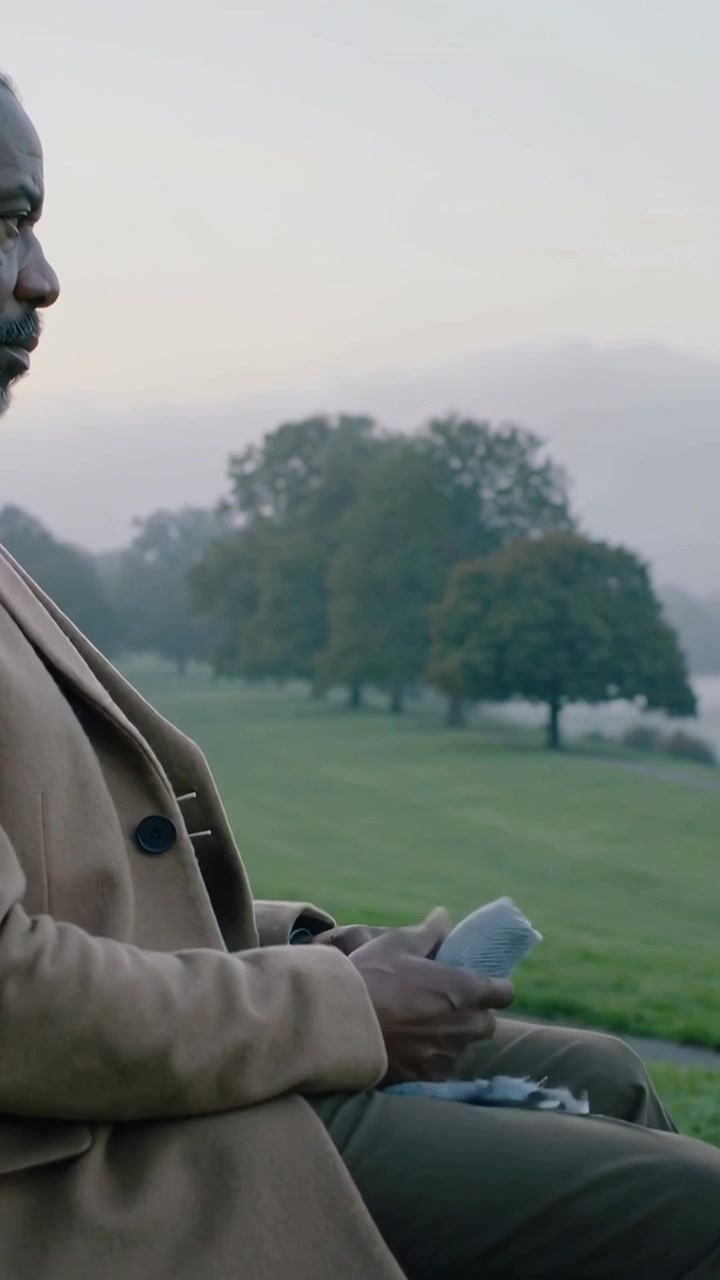 Vertical video: Pausing man in camel coat lifting scarf on park bench, opening to warm, copy space