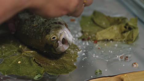 seasoning filleted fresh raw trout fish in tinfoil with herbs and salt