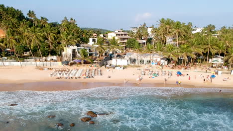 panorámica aérea de drones a lo largo de la concurrida playa de sri lanka al atardecer en la hora dorada.