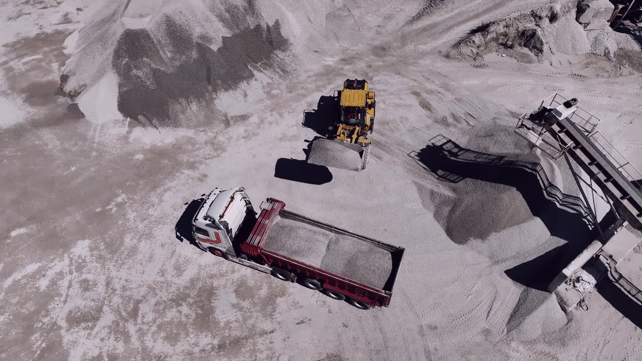 Aerial shot of an industrial loader filling a truck with gray sand at a quarry