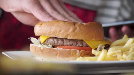 hand squashing cheese hamburger from fast food outlet, closeup